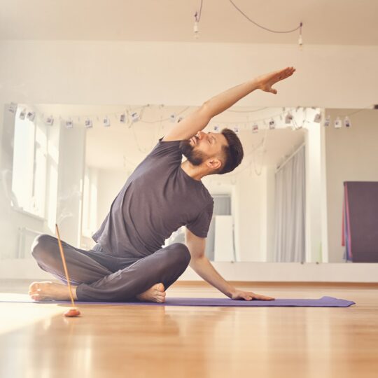 Handsome young man doing stretching exercise in yoga studio