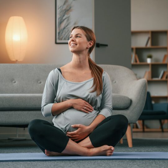 Sitting on the yoga mat. Beautiful pregnant woman is indoors at home